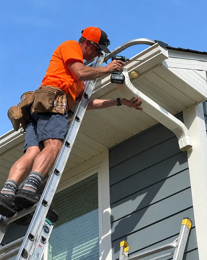 Brian Jacobsen on a ladder installing seamless aluminum gutters on a Twin Cities home roofline
