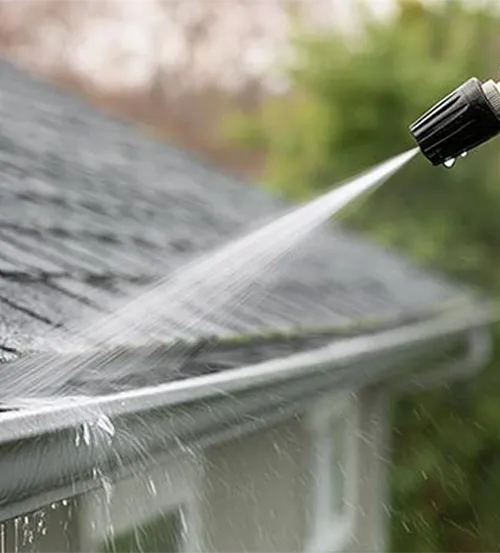 Flushing residential rain gutters with water hose sprayer to clear debris and check drainage flow